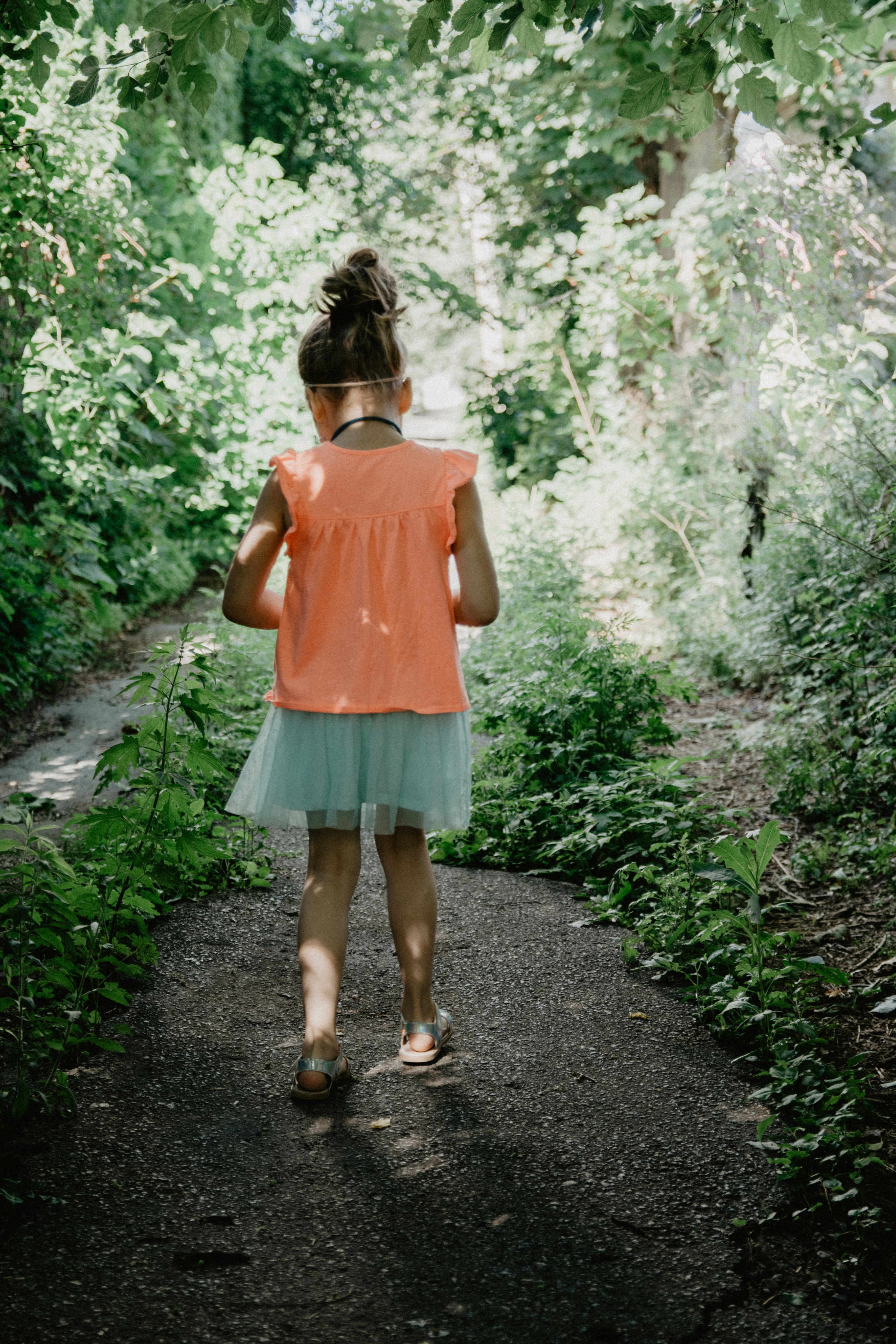 woman in pink tank top and blue denim shorts standing on pathway between green plants during